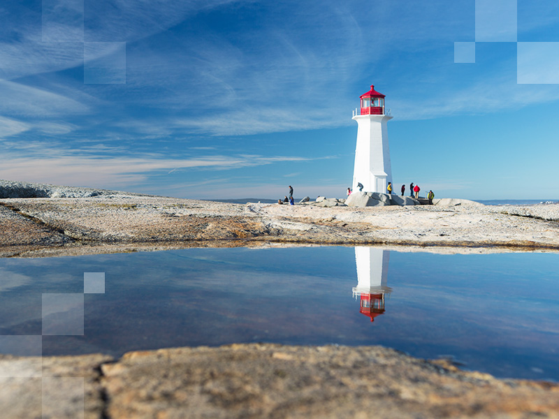 Image of Peggy's Cove Lighthouse with its reflection in a pool on the granite rocks, surrounded by tourists.